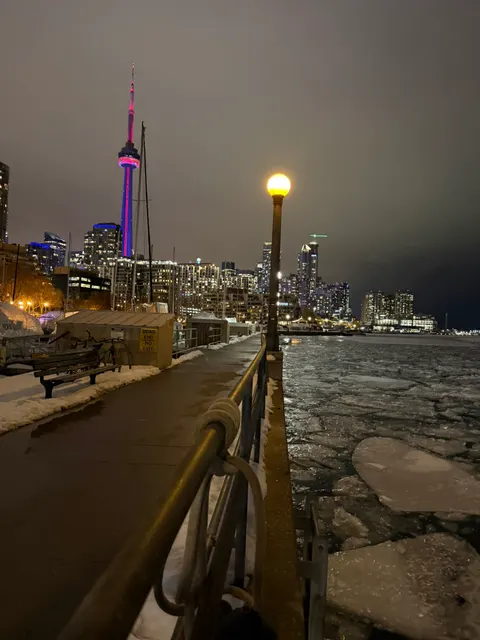 Toronto's CN Tower rises above an icy waterfront after sunset.