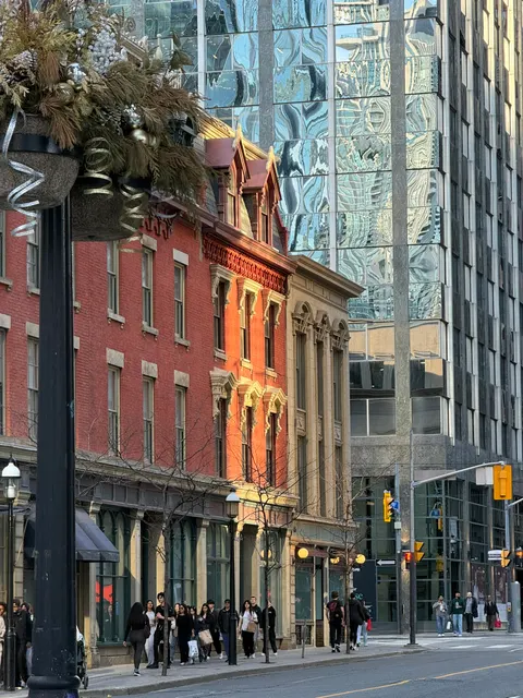 A red brick corner building stands beside a reflective glass tower in Toronto.