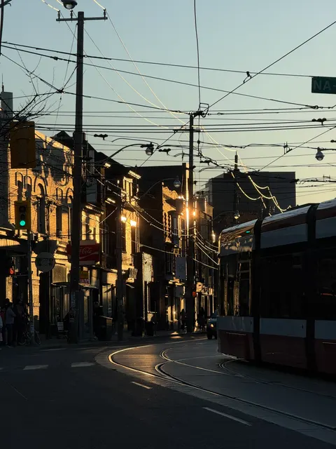 Streetcar wires cross above a quiet Toronto street in warm evening light.