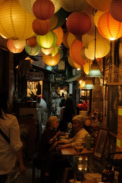 Warm lanterns illuminate diners in a narrow restaurant passage.
