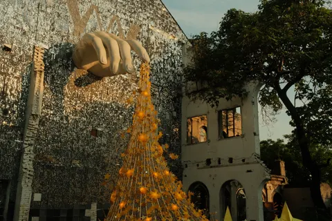 An orange hanging sculpture fills a brick courtyard between old buildings.