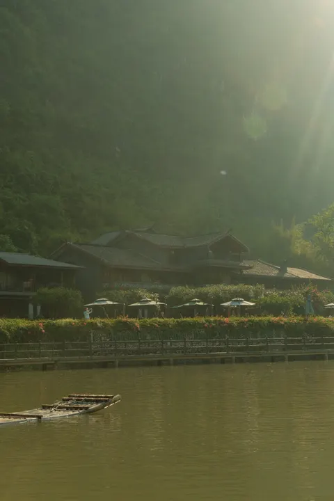Low buildings sit beside a still river under misty limestone peaks.