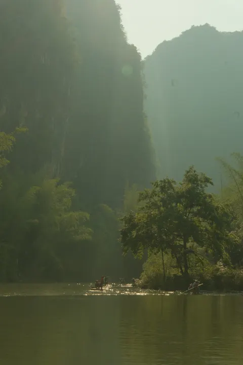 Layered limestone cliffs emerge from mist above a quiet river.