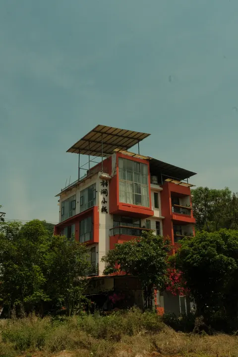 A red-trimmed house rises among trees beneath limestone hills.