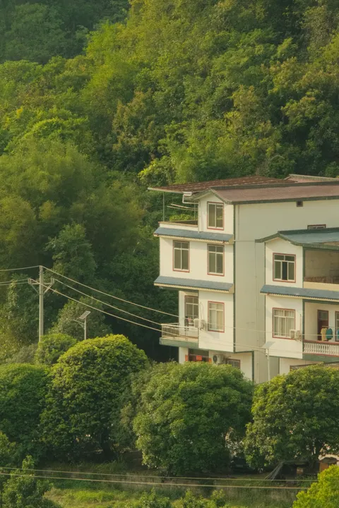 A white guesthouse sits among dense foliage beneath Yangshuo hills.