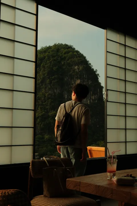 A visitor looks through a dark window toward a sunlit karst landscape.
