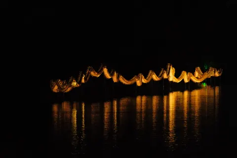Traditional rooflines glow in reflection across a dark river at night.