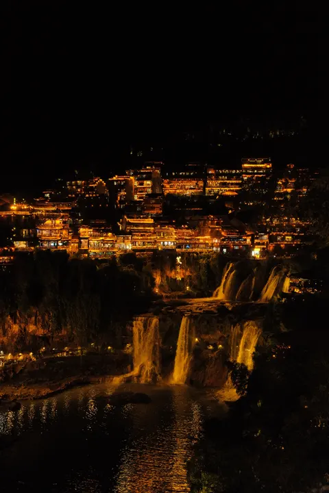A mountainside village glows gold across the Zhangjiajie valley at night.