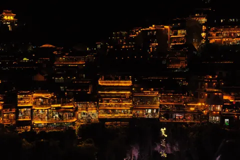 Warm lights trace a dense hillside settlement after dark in Zhangjiajie.