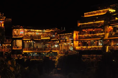 Traditional multi-story buildings glow amber on a nighttime hillside.