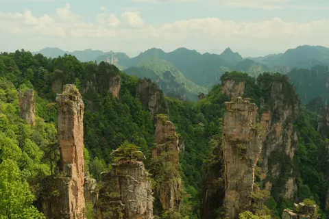 A solitary sandstone column stands among forested Zhangjiajie peaks.