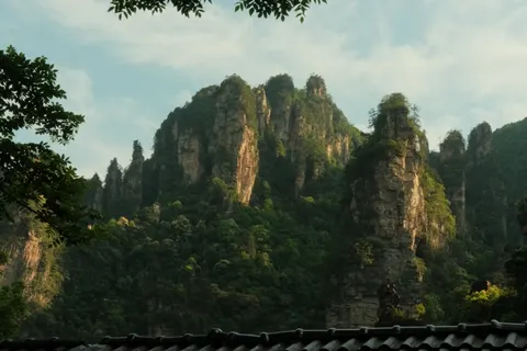 Jagged forested peaks rise beyond a tiled rooftop in Zhangjiajie.