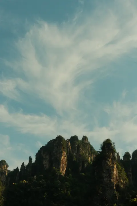 A rocky mountain silhouette reaches into a pale blue sky.
