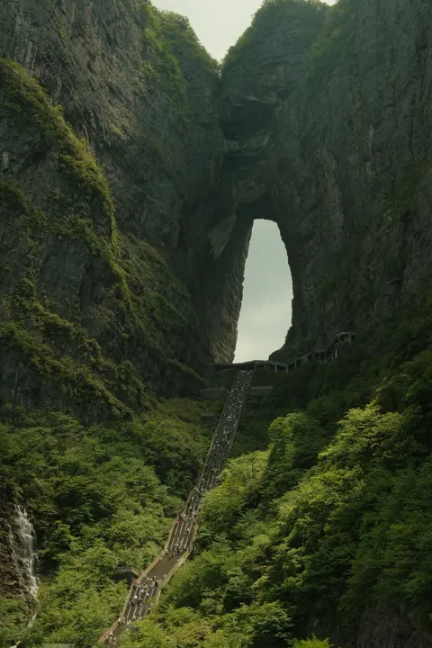 A natural stone arch opens through a forested mountain wall.