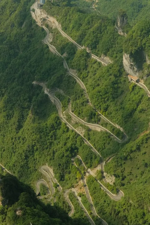 A winding mountain road crosses a deep forested valley.