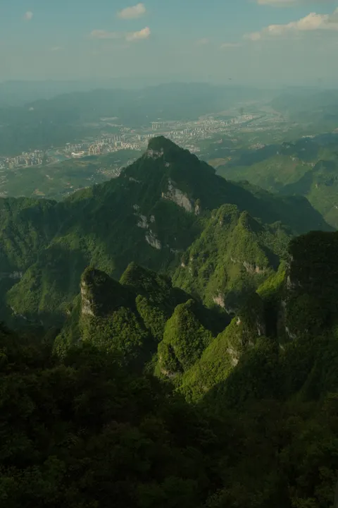 A jagged green ridge overlooks a distant lowland city.