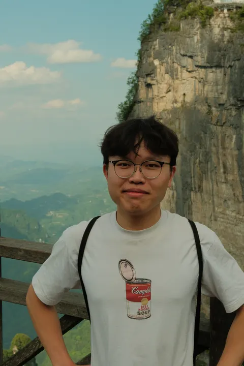 A smiling visitor poses beside a towering sandstone cliff.
