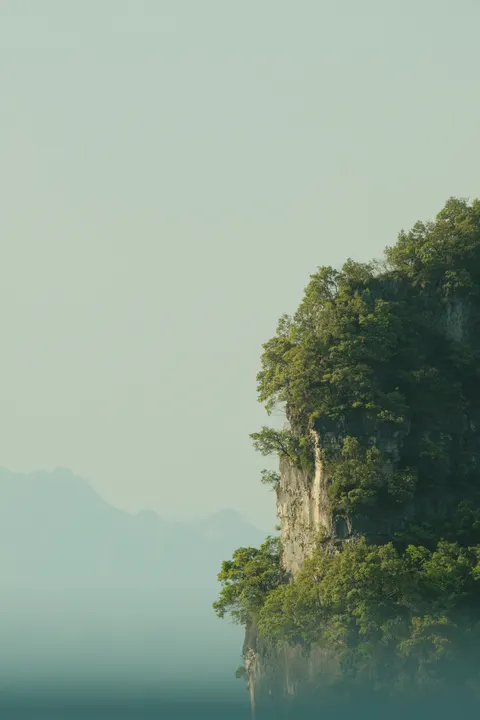 A hazy mountain island rises from a pale river gorge.