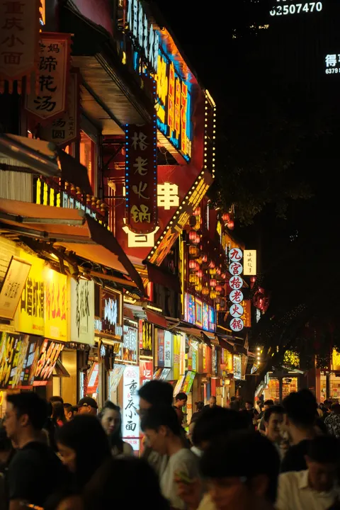 Dense neon signs tower over a crowded Chongqing shopping street.