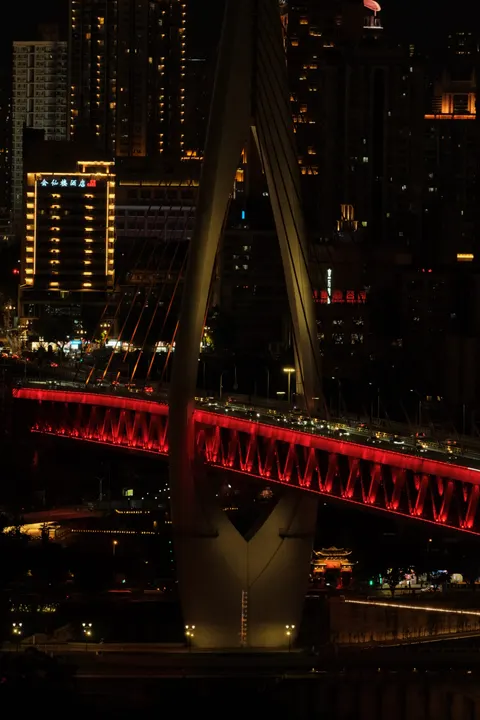 A red illuminated bridge spans the Chongqing night.