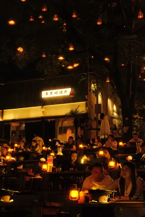 Diners gather beneath small red lights on a dark Chongqing terrace.