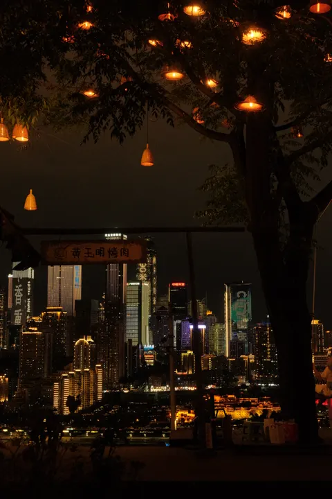 A tree strung with warm lights shades an outdoor restaurant at night.