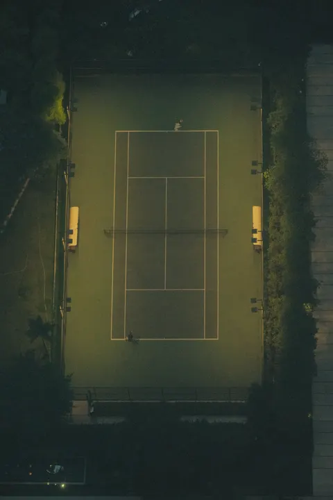 A green tennis court appears through a dark, misted window.