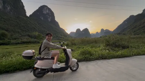 A scooter rider pauses on a country road surrounded by Guilin karst peaks.