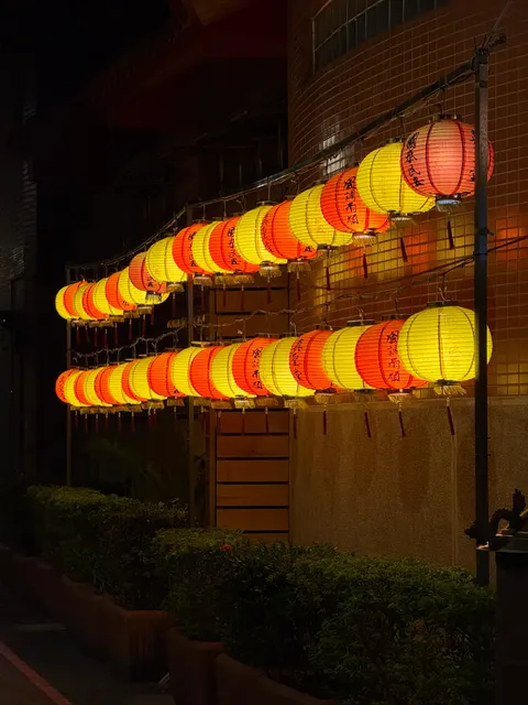 A row of red and yellow lanterns glows outside a Taipei building.
