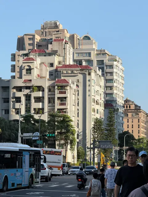 Pedestrians cross before sunlit apartment buildings in Taipei.