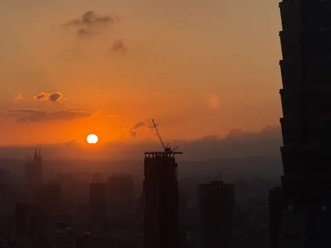 The sun sets through orange haze above Taipei construction cranes.