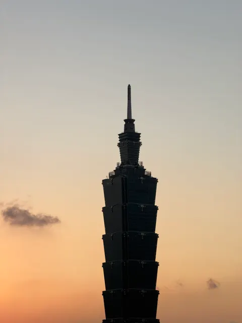 Taipei 101 forms a dark silhouette against a peach sunset.