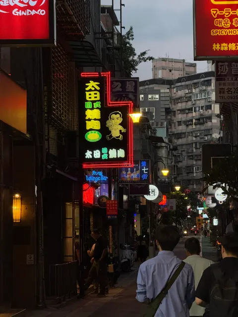 Vertical neon signs brighten a crowded Taipei night street.