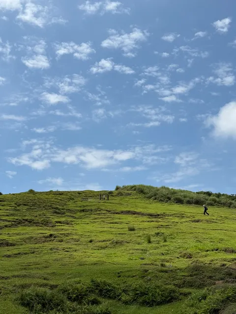 Visitors walk across a vivid green grassy ridge under blue sky.