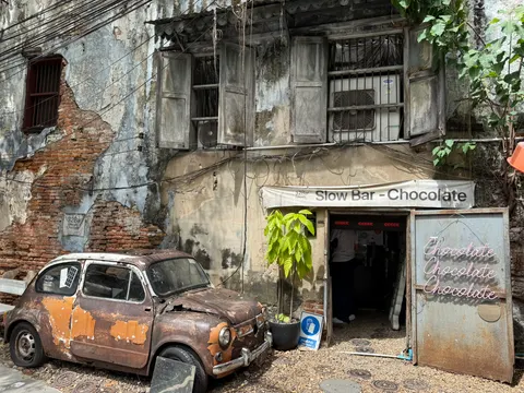 An old orange car rests outside a weathered Bangkok storefront.
