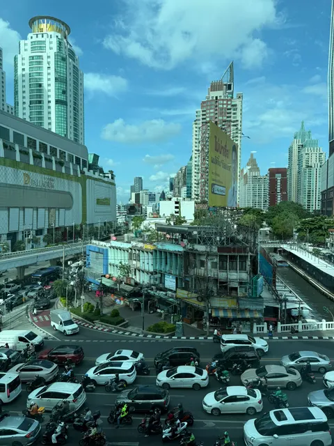 Traffic flows between modern towers on a bright Bangkok avenue.
