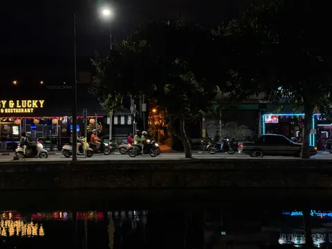 Streetlights reflect in a canal beside a Chiang Mai road at night.