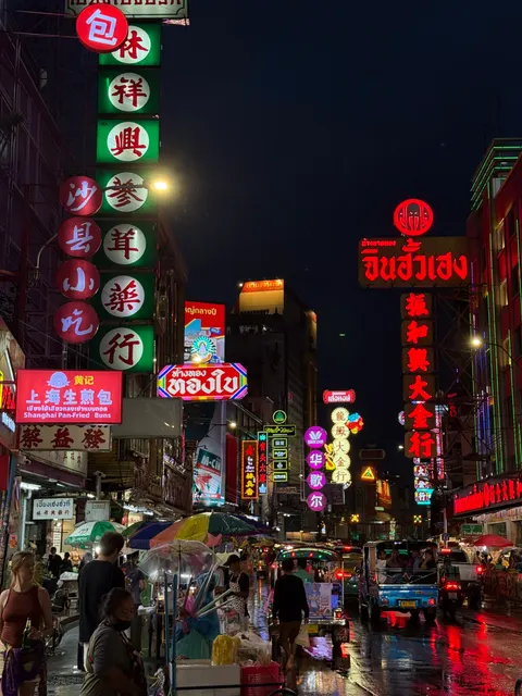 Red and green neon signs crowd a busy Bangkok street at night.