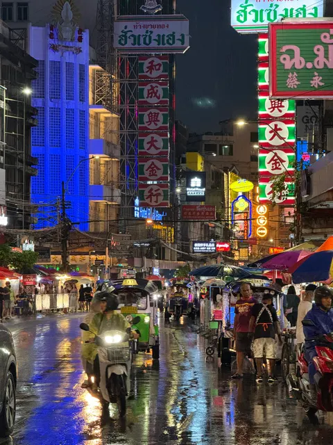 Rain-slick pavement reflects colorful signs in nighttime Bangkok.