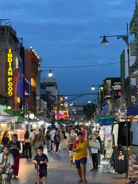 A crowded Bangkok shopping lane glows with signs after dusk.