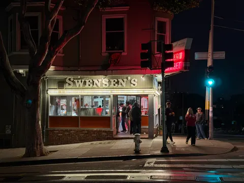 A red-lit corner shop glows on a San Francisco street at night.