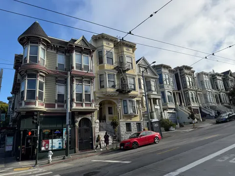 Victorian houses and storefronts line a sunny San Francisco block.