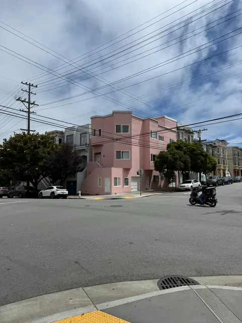 A pink building anchors a residential San Francisco street corner.