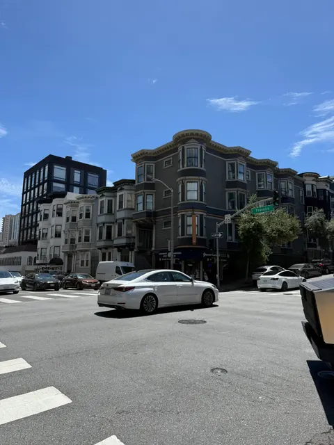 A white car passes ornate bay-windowed homes in San Francisco.